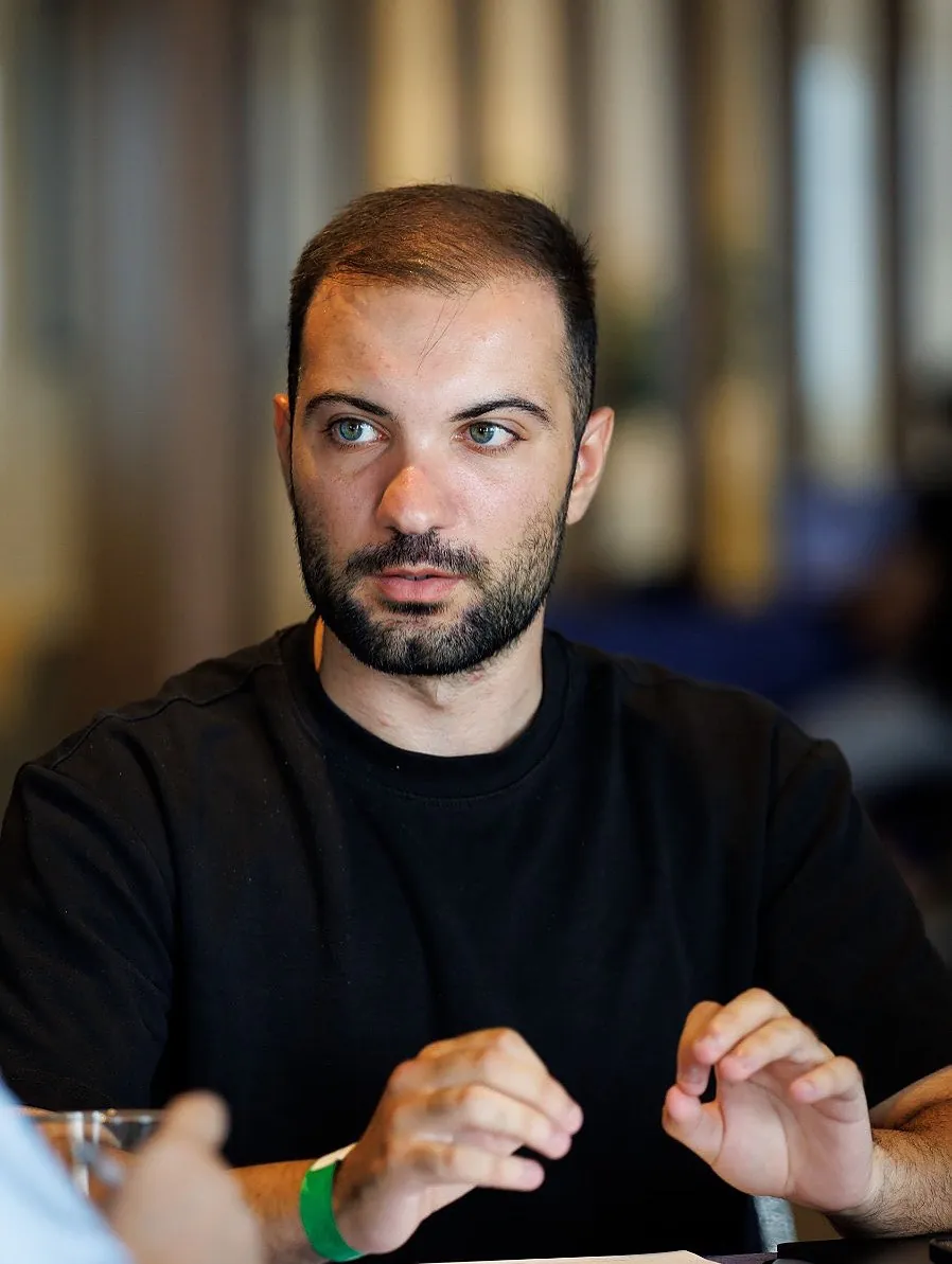 Matthew Mangion in a black t-shirt, mid-conversation at a table